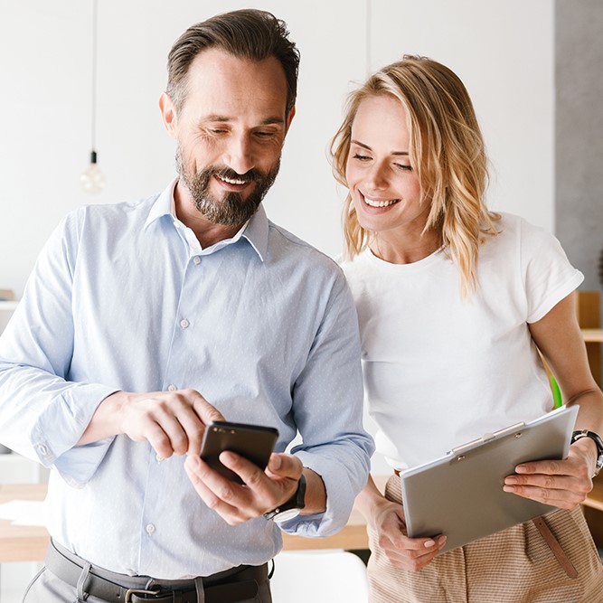 Couple of smiling colleagues looking at mobile phone
